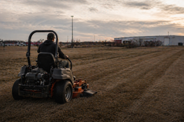 Man riding a lawn mower on grass near trees in a backyard