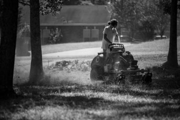 Person operating a stand-on lawn mower cutting grass outdoors