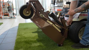 Operator using a PowerFold mower deck system to raise and access the underside of a zero-turn mower for blade inspection
